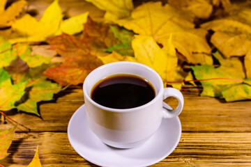 Cup of coffee and heap of yellow maple leaves on a wooden table