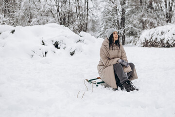 Fototapeta na wymiar Young woman having fun sitting on sled sleigh in winter snowy season in city park covered hill, holiday vacation weekend, enjoying spending time together
