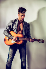 A shirtless man with an open jacket on nude torso, holding an orange guitar