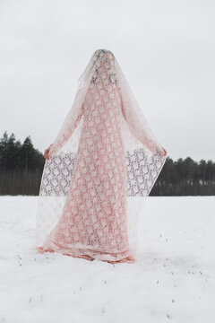 woman in pink dress standing in winter field of snow with veil