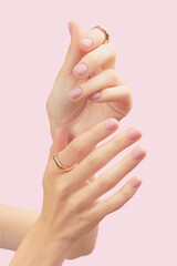 Beautiful groomed womans hands with pink matte nail design on a pink background