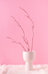 Painted wooden branch in white vase on a fluffy fur and pastel pink background. Holiday home decoration concept. Pink or white aesthetic.