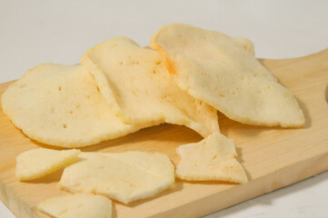 Three whole shrimp crackers and pieces of shrimp crackers on a wooden cutting board isolated on a white background