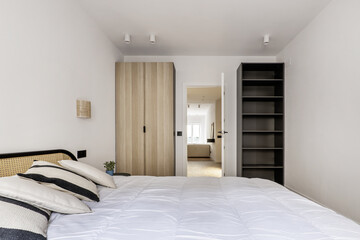 Fototapeta na wymiar Bedroom with double bed with cushions on the headboard, a wardrobe in one corner and a black shelf in the other