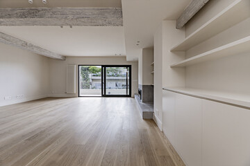 Living room of a recently renovated modern home with built-in furniture on one side, a gray fireplace at ground level and a terrace with views of the neighbors