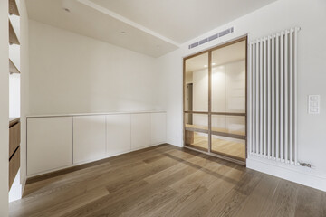 Corner of an empty modern living room with custom made furniture on one wall and a large white vertical steel radiator painted white