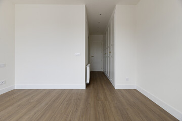 empty bedroom with white painted walls, white wooden access door in hallway with matching built-in wardrobes, wooden skirting boards and light wooden floors