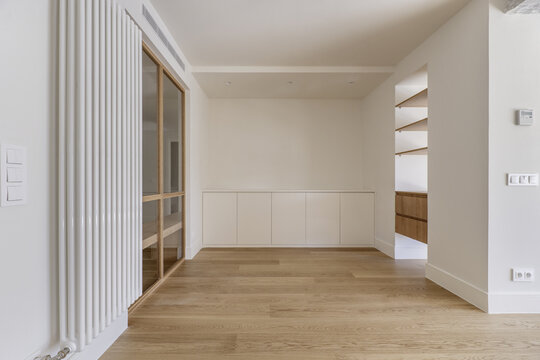 front image of an empty and modern living room with white painted walls and glass and wood partition, large vertical radiator and wooden floors