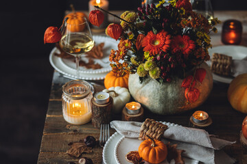 Fall composition. Orange pumpkins, flowers and candles on wooden table. Family elegant Thanksgiving or halloween dinner. Cozy autumn concept, simple handmade decoration, countryside style, wine