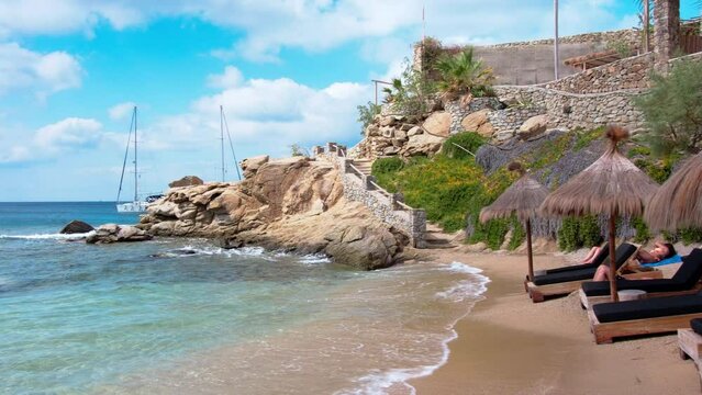 Paraside Beach in Mykonos, Greece, umbrella and luxury beach chairs beds in front of blue ocean. Most famous beach with crystal water and beach music bars. Gimbal cinematic ProRes graded from Log