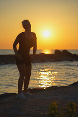 Fototapeta premium Silhouette of a sporty happy girl at sunset on the sea.