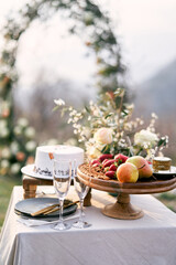 Fruit platter stands near glasses and wedding cake on the table