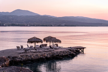 Sunrise by the sea in Isthmia, Greece, romantic beach dawn on holidays, pier with parasols