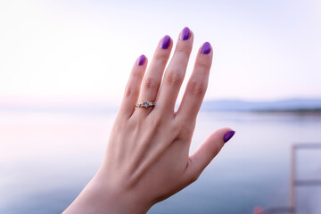 Woman's hand with a proposal diamond ring by the sea, sunrise on beach proposal, white sapphire golden ring - obrazy, fototapety, plakaty