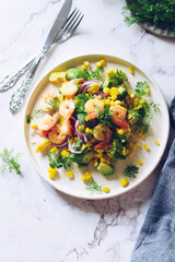 Healthy salad with fresh vegetables - corn, avocado, red onion, shrimp and coriander on a white plate.