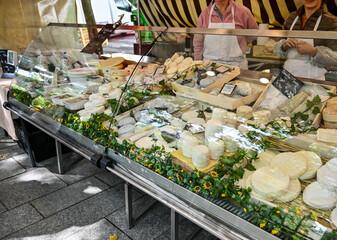 Paris, France. June 30 2022. At the beautiful local market Marché Popincourt, at a cheese counter with all the French specialties. The owners behind the counter. - obrazy, fototapety, plakaty