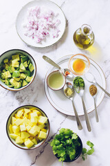 Ingredients for healthy salad with avocado, mango, red onion and green coriander on a black plate with lime and olive oil.