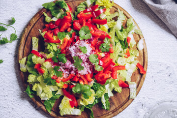 Healthy salad with fresh vegetables - salad romaine, red bell pepper, coriander and red onion on a wooden board