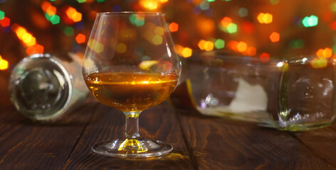 Glass of whiskey or brandy and empty bottles on wooden table on bright glowing background