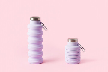 Collapsible reusable lilac water bottle on pink background. Sustainability, eco-friendly lifestyle