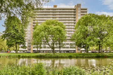an apartment building with trees and water in the fore - image is taken from across the pond to the...