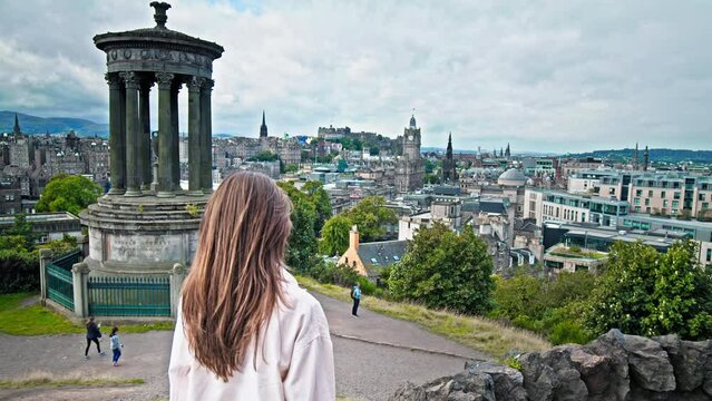Beautiful woman enjoying amazing view of Dugald Stewart Monument in Edinburgh, Scotland.Tourist girl visit Edinburgh city.