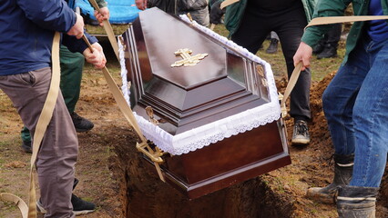 Burial. Men lower the coffin into the grave.