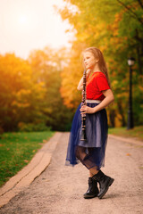 Young attractive girl playing clarinet, ebony in fall park