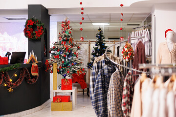 Empty festive clothing store during christmas season, beautifully decorated xmas tree and ornaments in fashion center boutique. Retail shop inside mall waiting for clients during holiday season.