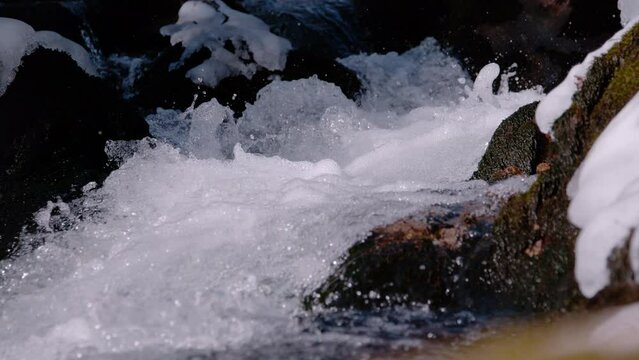 SUPER SLOW MOTION, CLOSE UP: Lively and splashing flow of a small mountain stream. Fresh spring water making its way between mossy and snow covered rocks. Calming view of free flowing clear water.