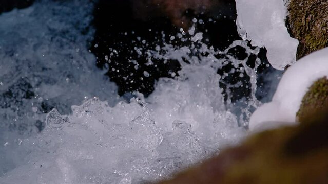 SUPER SLOW MOTION, CLOSE UP: Flying water drops of a splashing mountain creek. Fresh spring water making its way between mossy and snow covered rocks. Calming view of free flowing clear water.
