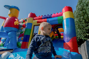 Fototapeta na wymiar blond boy Child jumping on a colorful trampoline in the park, running away from friends and pursuers to a secret place, Portrait of a happy child High quality photo
