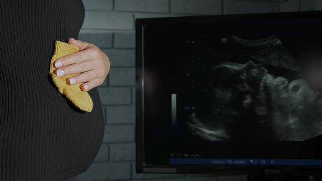 Socks by ultrasound baby embryo. A woman hold the socks for her future baby against ultrasound baby embryo picture.