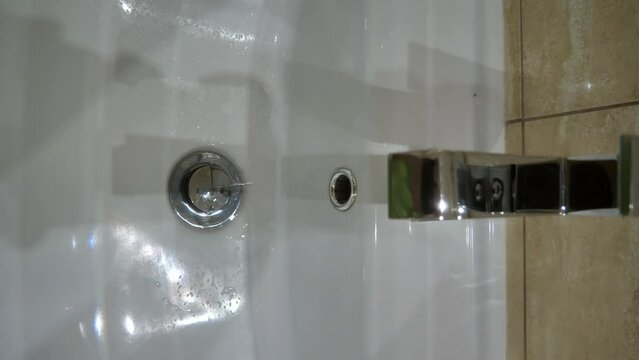 water drips into the sink from a faulty faucet with a drain plug. Outdated plumbing, broken faucet, leaking. Drinking water shortage. vertical video