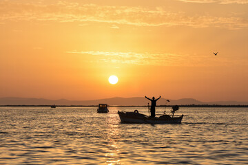 Fishing boat on a sea at sunset. A fisherman spread his arms wide