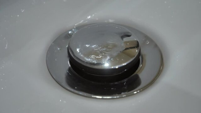 Close-up of water from a faulty faucet dripping into a sink with a drain plug. Outdated plumbing, broken faucet, leaking. Drinking water shortage