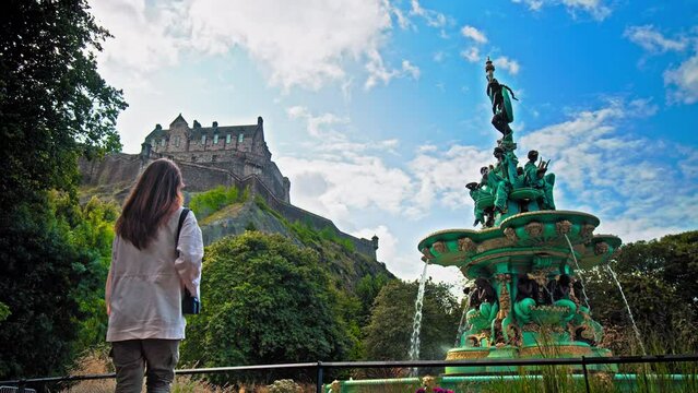 A beautiful woman visits Ross Fountain in Edinburgh, Scotland. Tourist girl looking at the Garden-side, cast-iron fountain representing science, arts, poetry and industry with Edinburgh Castle.
