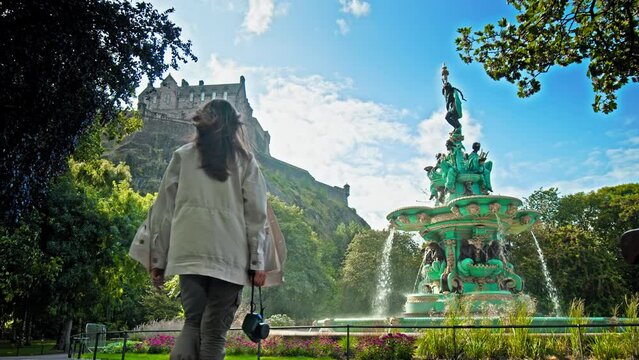 A beautiful woman visits Ross Fountain in Edinburgh, Scotland. Tourist girl looking at the Garden-side, cast-iron fountain representing science, arts, poetry and industry with Edinburgh Castle.
