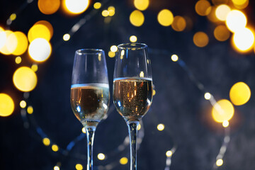 Two glasses of sparkling champagne on a Christmas background with a garland of bokeh