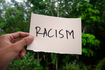 Hand holding white Paper with racism text in solative on nature background. Racism concept. Discrimination, racial issues