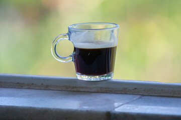 Transparent glass cup with black coffee on the window