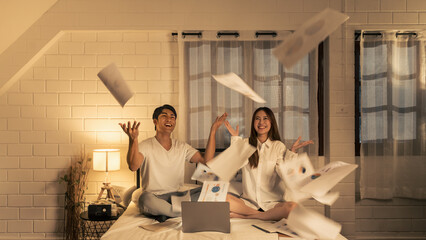 joyful asian couple celebrating success with financial graphs and business reports papers flying in...
