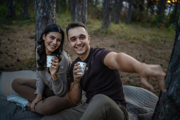 Young couple man and woman boyfriend and girlfriend or husband and wife in love relationship hold paper cup of coffee or tea while spend time together in the park forest bonding love real people