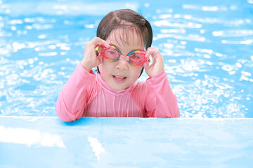 Happy little Asian child girl in swimming suit at swimming pool