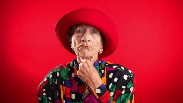 Portrait of funny elderly senior old woman with no teeth and wrinkled skin looks at camera gives great idea gesture showing explosion of thinking posing isolated on red background