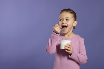 Girl eating tasty yogurt on violet background, space for text