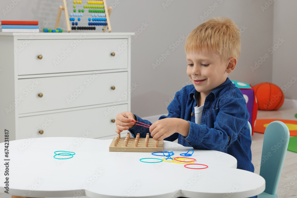 Canvas Prints Motor skills development. Boy playing with geoboard and rubber bands at white table in room