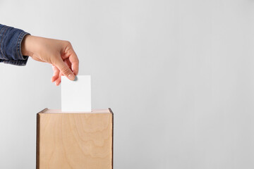 Fototapeta na wymiar Woman putting her vote into ballot box on light grey background, closeup. Space for text