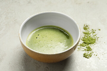 Cup of fresh matcha tea and green powder on light grey table