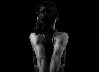 Strong sporty woman doing the arms and shoulders stretching exercise holding the hands in fist behind the back to relaxing back side of body in sport wear. Closeup - obrazy, fototapety, plakaty